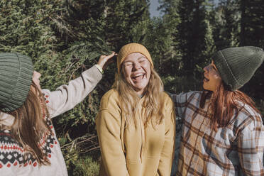Frauen stecken einen Fichtenzweig in die Strickmütze einer glücklichen Freundin im Wald - VBUF00204