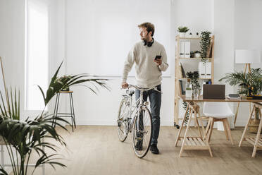 Geschäftsmann mit Fahrrad und Smartphone im Büro - EBBF06731