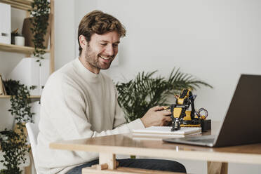 Smiling engineer working on robotic model arm in office - EBBF06745
