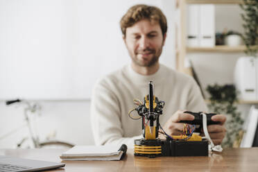 Engineer operating robotic model arm holding pen on desk in office - EBBF06748