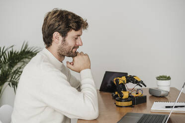 Engineer examining robotic arm on desk in office - EBBF06751
