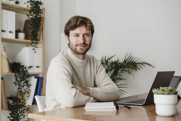 Businessman with arms crossed at desk in office - EBBF06761