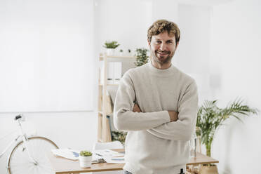 Smiling businessman with arms crossed standing in office - EBBF06769