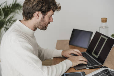 Geschäftsmann tippt auf einem Laptop am Schreibtisch am Arbeitsplatz - EBBF06773