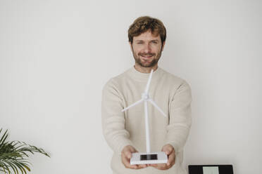 Businessman with wind turbine model in front of white wall - EBBF06778