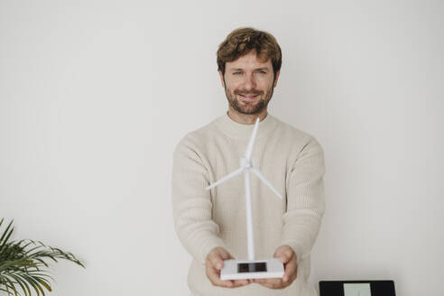 Geschäftsmann mit Windturbinenmodell vor einer weißen Wand - EBBF06778