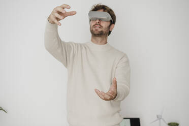 Geschäftsmann mit VR-Brille gestikuliert vor einer weißen Wand - EBBF06781