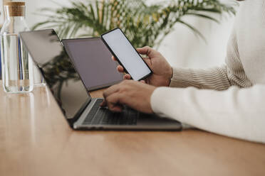 Hands of businessman using laptop and smart phone with blank screens at office - EBBF06790