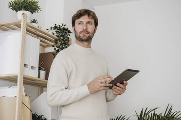 Nachdenklicher, gut aussehender Geschäftsmann mit Tablet-PC im Büro - EBBF06794