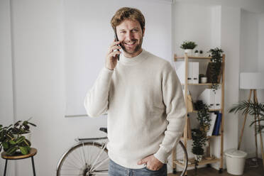 Lächelnder Geschäftsmann, der im Büro mit seinem Handy telefoniert - EBBF06805