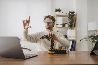 Engineer with VR Goggles gesturing by robotic arm at office - EBBF06807