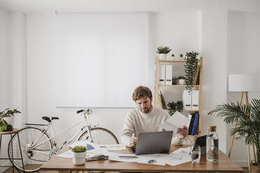 Engagierter Geschäftsmann bei der Arbeit an Diagrammen und Statistiken über einem Laptop am Arbeitsplatz - EBBF06811