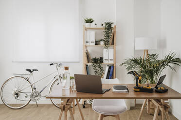 Moderne Technologien auf dem Schreibtisch mit Fahrrad und Gestell im Hintergrund im Büro - EBBF06825