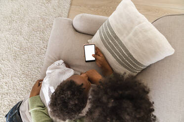 Mother and son with mobile phone lying on sofa at home - VPIF07649