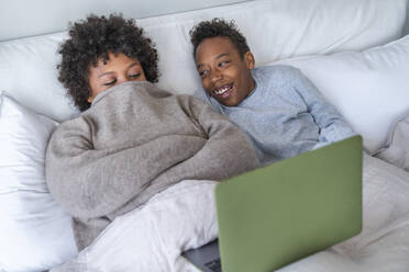 Mother and son spending leisure time with laptop lying on bed at home - VPIF07666