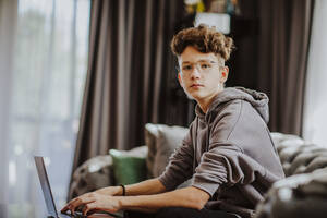 Jugendlicher mit Laptop, der zu Hause auf dem Sofa sitzt - MDOF00166