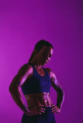 Monochromes Porträt einer muskulösen Sportlerin, die mit den Händen auf der Hüfte auf einem lila Hintergrund steht. - JLPSF19404