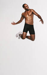 Bare chested athlete jumping high in air during workout. African american man doing fitness training. - JLPSF19427