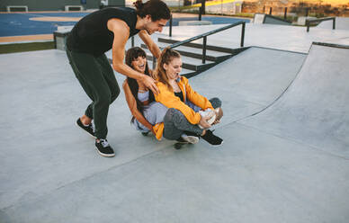 Eine Gruppe von Freunden hat Spaß mit einem Skateboard im Skatepark. Ein junger Mann und zwei Mädchen spielen mit einem Skateboard im Skatepark. - JLPSF19439