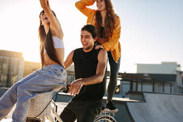 Happy man and women having fun riding a bicycle on a sunny day. Man riding a bicycle with a female friend sitting on the handle and another standing in back. - JLPSF19444