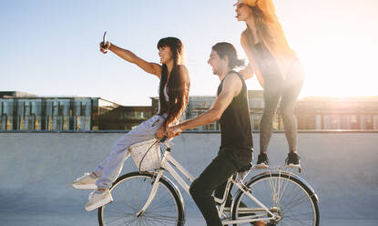 Friends on bike posing for a selfie. Young man sitting on bike with female friends on a sunny day. - JLPSF19447