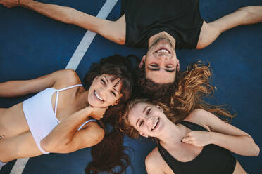 Top view of three friends lying no basketball court and laughing. Group of man and women lying together with their heads touching. - JLPSF19453