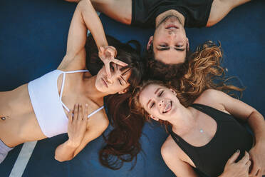 Directly above shot of young people lying down on ground and making funny faces. Group of man and women lying together with their heads touching and looking at camera. - JLPSF19454