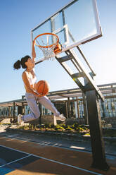 Eine Frau spielt Basketball im Freien an einem Sommertag und macht einen Slam Dunk. - JLPSF19458