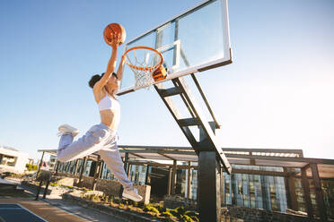 Frau Basketballspieler Slam Dunking auf Straße Gericht. Weibliche spielen Basketball im Freien auf Sommer Tag. - JLPSF19460