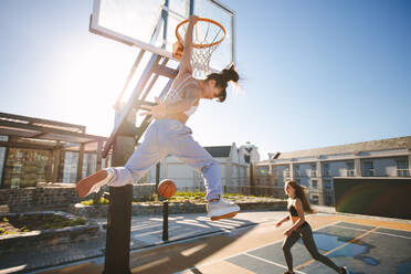 Zwei junge Frauen spielen an einem sonnigen Tag auf einer Straße Basketball. Frauen spielen im Freien Streetball. - JLPSF19462