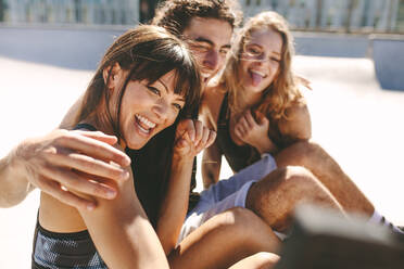 Group of friends posing for a selfie outdoors. Smiling woman taking a selfies while hanging out with friends outdoors. - JLPSF19485