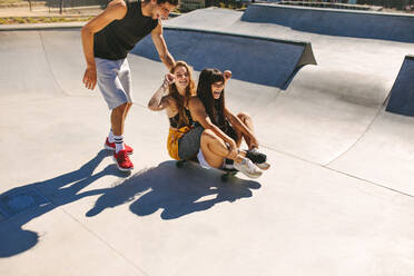 Eine Gruppe von Freunden hat Spaß im Skatepark. Ein junger Mann und zwei Mädchen spielen mit einem Skateboard im Skatepark. - JLPSF19488