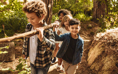 Eine Gruppe von Kindern spielt im Wald und sammelt Stöcke, um ein Lager im Wald zu errichten. - JLPSF19496