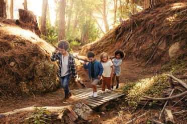 Eine Gruppe von Kindern baut gemeinsam ein Lager im Wald auf. Jungen und Mädchen tragen Stöcke und gehen - JLPSF19497