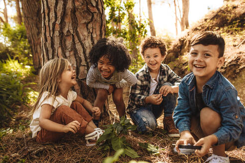 Eine Gruppe niedlicher Kinder, die zusammen im Wald sitzen und in die Kamera schauen. Niedliche Kinder spielen im Wald. - JLPSF19501