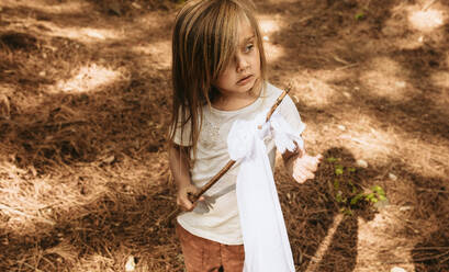 Niedliches Mädchen mit Stock und Tuch im Wald stehend und wegschauend, Kind spielt im Wald. - JLPSF19502