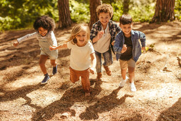 Eine Gruppe von Kindern rennt im Wald herum. Multi-ethnische Kinder spielen zusammen im Wald. - JLPSF19509