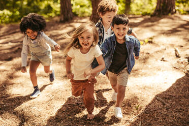 Eine Gruppe von vier Kindern, die zusammen im Wald rennen. Die Kinder machen ein Rennen, um einen Waldweg hinaufzuklettern. - JLPSF19510