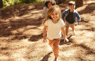 Cute girl running up hill in a park with friends. Group of kids playing together in forest. - JLPSF19512