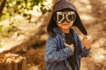 Cute boy with pilot goggles and hat. Kid dreaming to be pilot playing in forest. - JLPSF19514