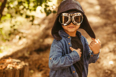 Niedlicher Junge mit Pilotenbrille und Hut, der davon träumt, Pilot zu werden und im Wald spielt. - JLPSF19514