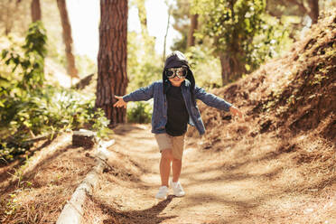Cute boy with pilot goggles and hat running in forest. Kid pretending to be pilot playing in forest. - JLPSF19515