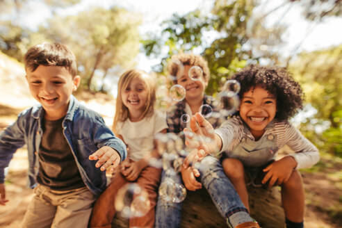 Eine Gruppe von Kindern spielt im Freien mit Seifenblasen, und die Freunde versuchen, die Seifenblasen zu fangen. - JLPSF19524