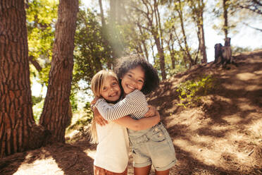 Two girls hugging each other outdoors. Kids together in forest having a great time. - JLPSF19530