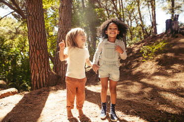 Lächelnde Mädchen, die sich im Wald vergnügen, Kinder, die gemeinsam im Freien springen. - JLPSF19531