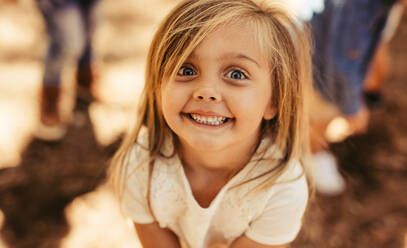 Close up Porträt von lächelnden adorable Mädchen mit Freunden im Hintergrund. Mädchen Kind schaut in die Kamera mit toothy Lächeln. - JLPSF19537