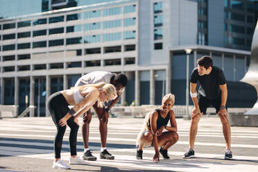 Multi-ethnic street runners taking a break after workout outdoors. Fitness group resting and smiling after running exercise in the city - JLPSF19571