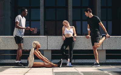 Multi-ethnic friends relaxing outdoors on the city street after workout. Group of men and women resting after workout. - JLPSF19572