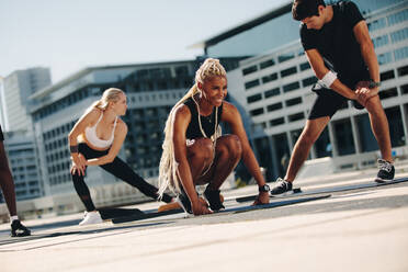 Group of people exercising together outdoors in the city. Multi-ethic men and women in sportswear doing stretching exercising. - JLPSF19575