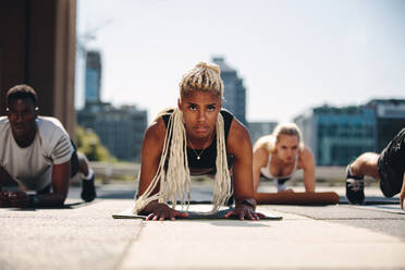 Eine Gruppe von Menschen macht eine Plank-Übung auf einer Fitnessmatte im Freien. Sportliches Gruppentraining in der Stadt. - JLPSF19579